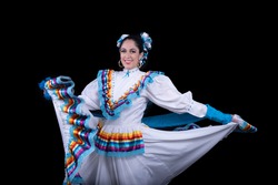 Latin woman dressed in a dress from Jalisco Mexico, white skirmish with ribbons of bright colors, braids and in movement skirt and smile, black background