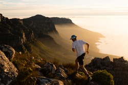 A trail running running along a challenging mountain trail at sunset in the mountains of Cape Town.