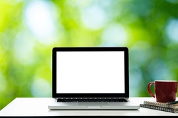 Empty space on white desk with Laptop with blank screen,at Grean blurred background of bokeh.