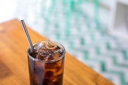 Close up on a tumbler glass full of diet cola and ice, with a reusable metal drinking straw, on a wood restaurant table 
