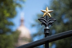 Macro close up on a decorative gold lone star on a wrought iron fence, with a spire dome building in the blurry background