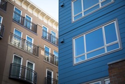 Wide angle close up on a modern blue apartment building, and a brown stucco hotel with balconies in the background