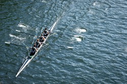 Top down view on a four person crew team, racing a rowing shell on a calm blue lake, with space for text on right