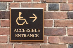 Close up on a bronze wheelchair and handicapped accessible entrance sign, on a brick wall