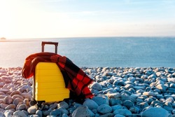 Yellow Suitcase with orange scarf on seaside. Travel concept.