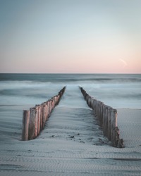 Calm sunset over beach in Netherlands. Waves slowly crashing into the jetty