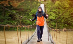 Man with backpack trekking in forest by hinged bridge over river. Cold weather. Autumn hiking. Wooden bridge across the river, Suspension bridge