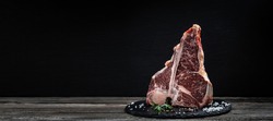 raw porterhouse steak or Fed T Bone Steak dry aged of beef Ready to Cook on wooden Board with herbs, pepper and salt.