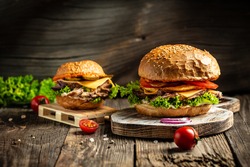 Tasty grilled homemade burgers with beef, tomato, cheese, bacon and lettuce on rustic wooden background. fast food and junk food concept.