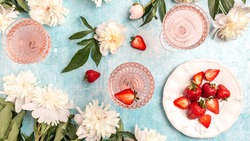Rose wine in glasses with Peony Flowers and sweet fresh strawberries on blue background, Summer drink for party, wine shop or wine tasting concept.