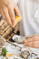A man's hands squeezes fresh lemon juice onto an raw opened oyster, lifestyle food, ready to eat. Oyster dinner with champagne in restaurant.