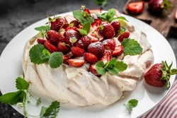 Homemade delicious meringue cake Pavlova with whipped cream, fresh strawberries and mint on wooden background, place for text, top view.