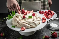 delicious homemade Pavlova cake with fresh strawberries and whipped cream. Female baker decorating delicious meringue cake, top view. place for text.