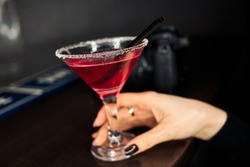 A glass of a cosmopolitan in woman`s hand. Pink alcoholic cocktail.  Blurred photo camera on dark background