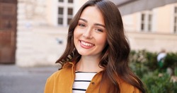 Portrait of Caucasian beautiful young woman looking at camera and smiling joyfully. Female beauty concept. Outside in town street. Close up of face of pretty girl with cheerful happy face.