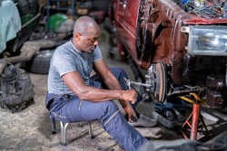 Mechanical man sitting concentrate use wrench to repair car front tire drum brake pad at the car repair shop