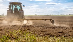 The farmer drove a plow to improve the soil, preparing for the upcoming cropping season on dry ground until the dust was dispersed in the air.