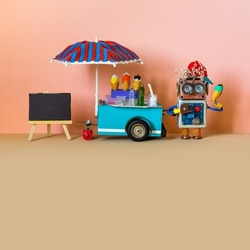 Toy ice cream cart shop and robot seller. A funny smiling robotics shopman with ice cream. Empty black chalkboard for menu. Summer time peach color background