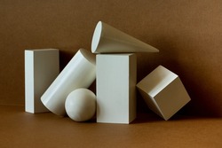White platonic solids figures geometry. Abstract geometrical objects still life composition. Three-dimensional rectangular prism, cylinder pyramid cube, sphere on brown background.