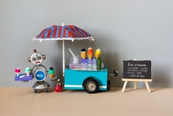 Ice cream mobile shop cart, black easel cafe menu. Toy store with big umbrella. Robot sell ice cream and cold lemonade. Sandy gray beach background.