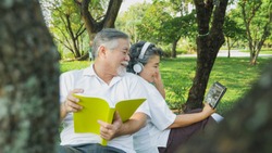happy senior couple listening to earphone with digital tablet and read book relax in park, People lifestyle concept.  