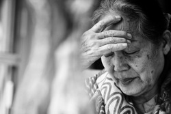 Black and white Image of 60s or 70s  Asian elderly woman facepalm or cover her face by her hands .She may had Headache Symptoms.She looks pain or sick or crying.Sad elderly or self isolated concept.