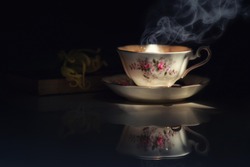 Still life image of  hot tea cup in the dark with Cananga odorata  or Ylang-ylang flower put on old book.Light pass through, shadow touch up the scene.Concept of simple or relax moment with tea.