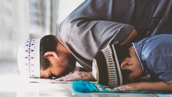 Religious Asian Muslim Man teaching his little son to pray to God in Sujud. The position involves having the forehead, nose, both hands, knees,all toes touch to ground.to praise and glorify Allah.