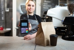 Contactless payment of an order through a payment terminal with nfs to a barista girl in a cafe for coffee and food in paper packaging.The girl holds out the device to pay for the order.coffee concept