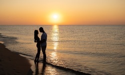 A couple in love is experiencing romantic tender moments at sunset on the beach. Young lovers on summer vacation. concept of love or honeymoon. Kiss in silhouette at sunset. copy space. banner