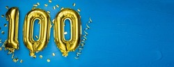 golden yellow foil balloon on blue concrete background number one hundred. Birthday or anniversary card with 100 inscription. Anniversary celebration. Banner.