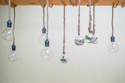 Decorated cozy lamps stick in the rope and little tiny tree with small white rock inside the ball glass hang on to big wood log in front of white background.