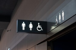 A sign of restroom lighten in white standout from a black plate. The restroom is inside a building, decorated in black and white tone.