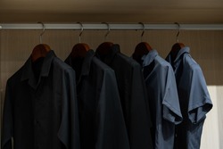 Shirts hang in a walking closet with glass door. Two of those is in dark blue standout from others that are in black.