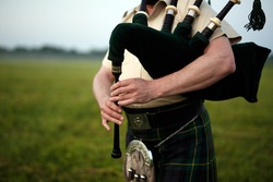 A musician plays the bagpipes in the fields. Fingers and bagpipe close up.
