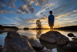A silohuette of a child at a lake at sunset with reflections