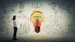 Side view of a pensive young woman looking at the wall with colorful light bulb and business sketch. Uniqueness of the idea and genius concept.