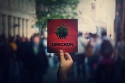 Omicron the new variant of the Covid-19 virus, coronavirus mutations, sars-cov-2 strain. Hand holds red banner warning in the crowded streets. Another wave of pandemic outbreak