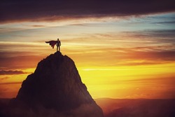 Businessman superhero conceptual scene. Determined hero with red cape stands brave on a mountain peak. Business leadership, ambition and strength metaphor. Overcome obstacles and achieve success