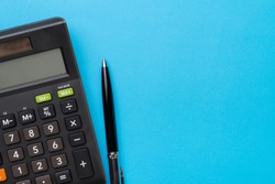Financial activity, accounting, tax calculation or saving and investment, black calculator with pen on solid blue background with copy space.