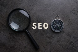 Magnifying glass, alphabet SEO and compass on dark cement background using as SEO Search engine optimization concept.