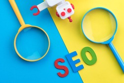 SEO Search engine optimization concept with blue and yellow magnifying glass, alphabet abbreviation SEO and robot on colorful background.