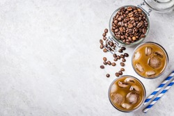 Cold brewed iced coffee in glass and coffee beans in glass jar on white background. Top view, copy space.