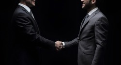 Two cheerful businessman shaking hands and looking at each other