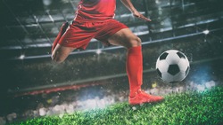 Close up of a soccer scene at night match with player in a red uniform kicking the ball with power