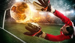 Close up of a soccer scene at night match with a goalkeeper trying to catch a fiery ball
