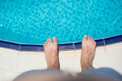 Pair of feet standing on stone border in front of swimming pool.