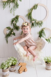 a little girl in a wreath. the child sits on a white background. baby in a green wreath. rustic style. young child