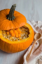 oatmeal, porridge with pumpkin inside bright big orange squash, close up view, autumn breakfast, soft selective focus