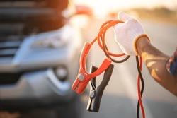 Car broken on the road. Man holding red and black battery cable for charging the car. Car Repair and maintenance concept